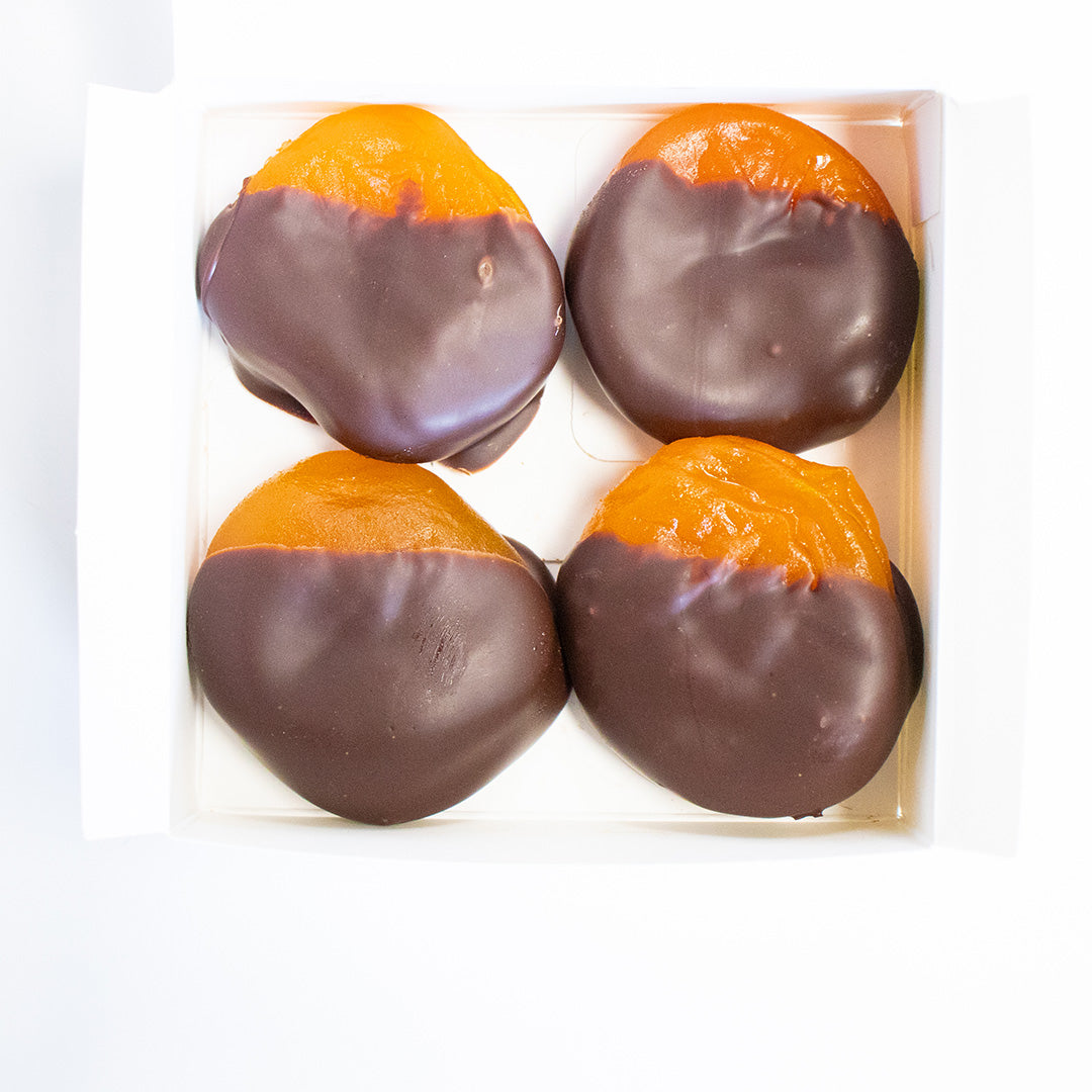 Four chocolate-dipped orange fruits in a clear packaging on a white background