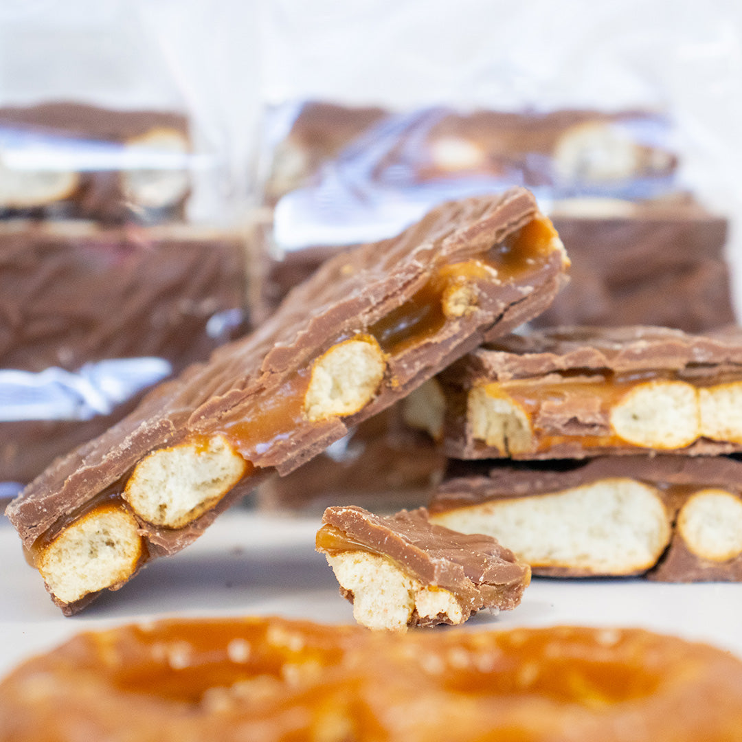 Chocolate-covered pretzel sticks with caramel bits on a white surface.