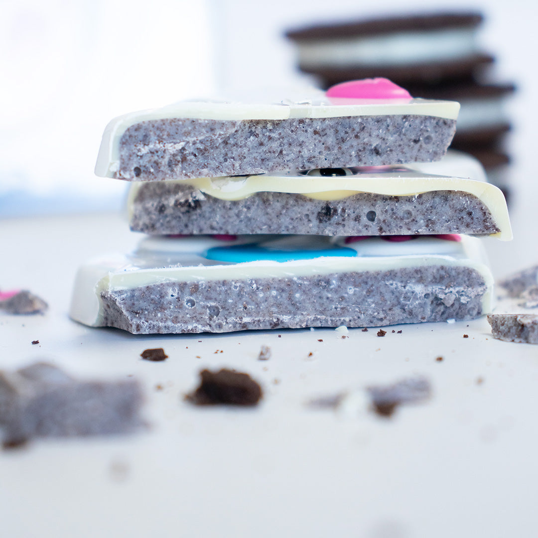 Stack of layered cookie dough bars with white and chocolate coatings on a light background