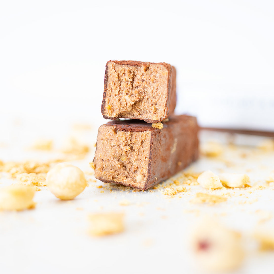 Two pieces of chocolate-covered cookie dough on a white background with crumbs around.