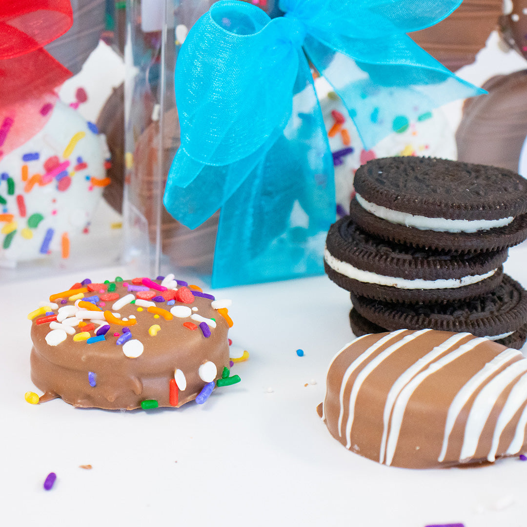 Decorative cookies with colorful sprinkles, chocolate, and a stack of Oreo cookies on a white surface.