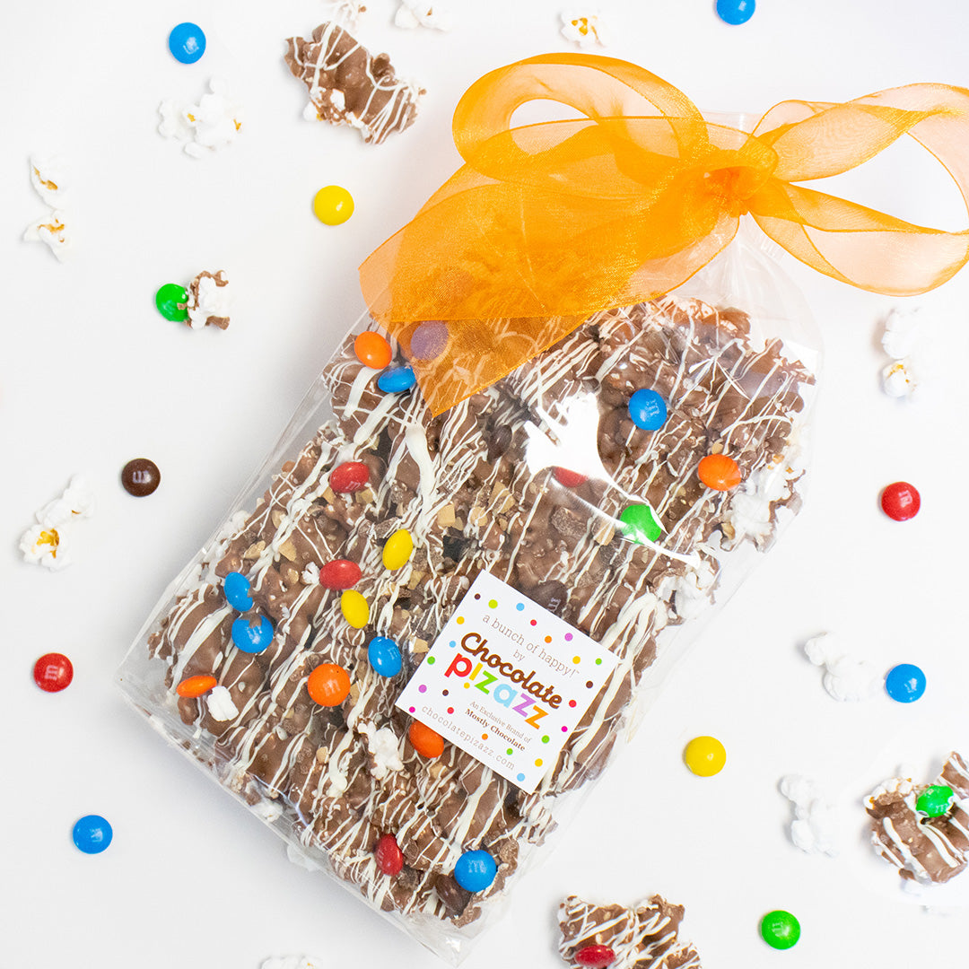 Packaged chocolate treat with colorful candies and an orange ribbon on a white background