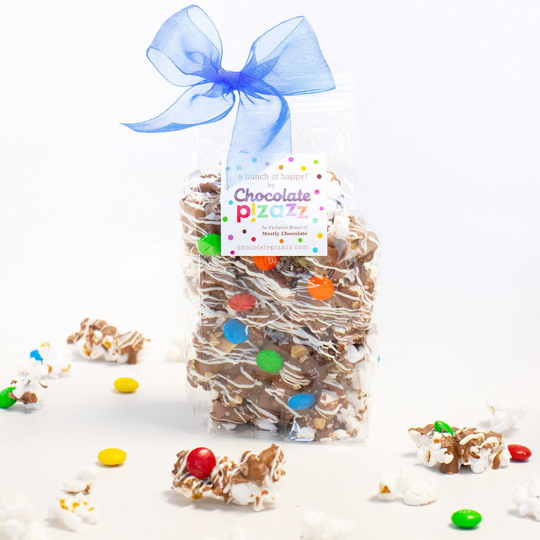 Bag of chocolate-covered popcorn with colorful candies and a blue bow on a white background