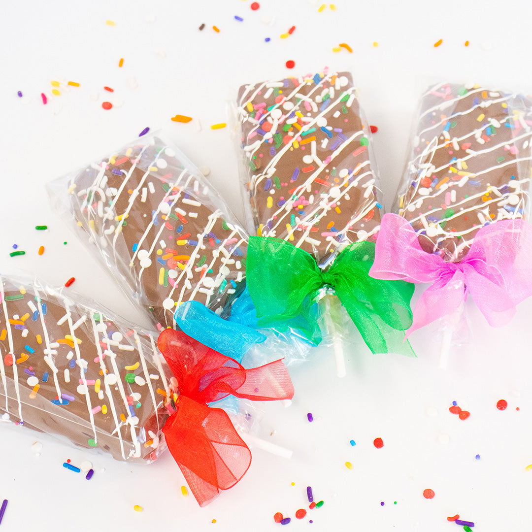 Three chocolate-dipped treats with colorful sprinkles and bows on a white background