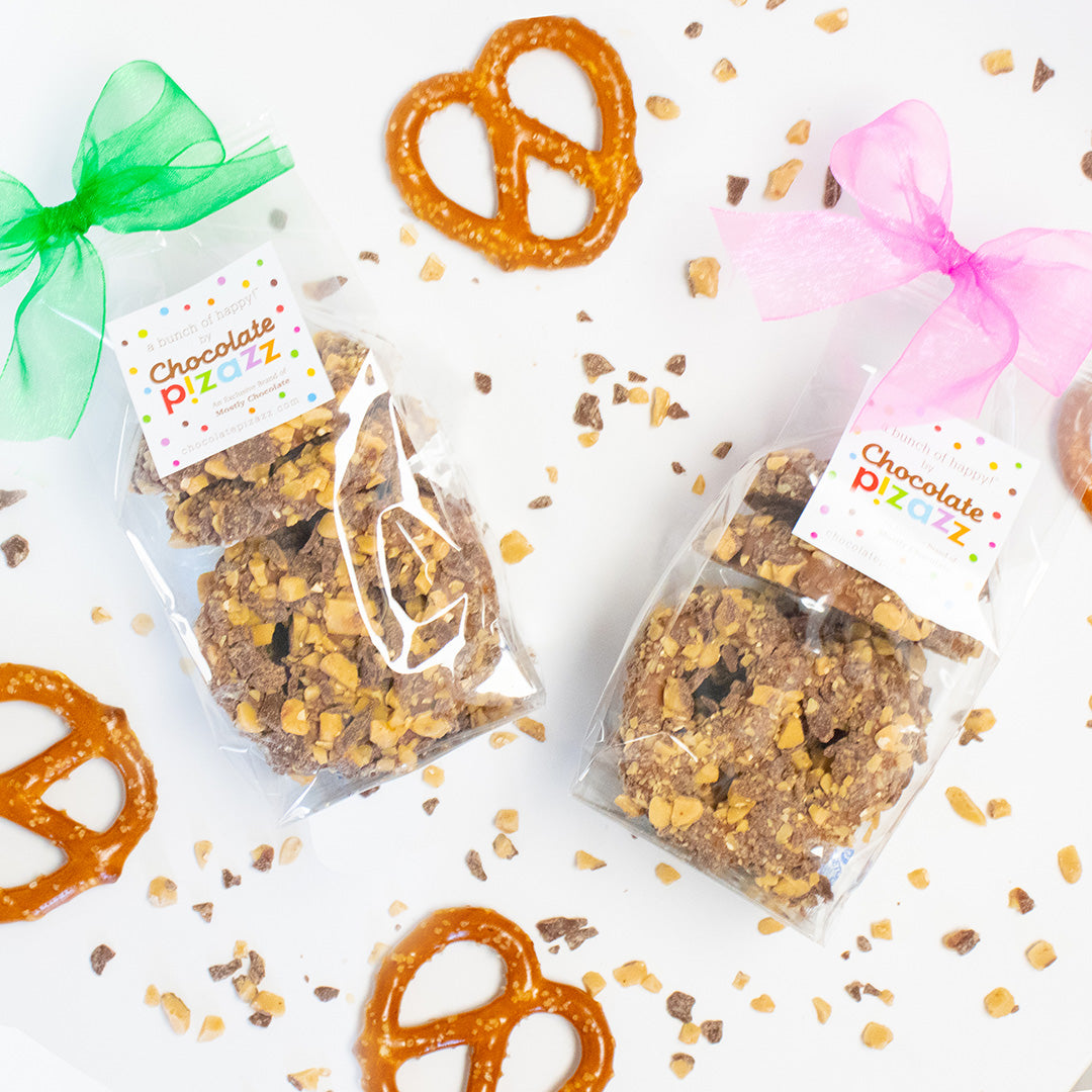 Two packages of chocolate-dipped pretzels with colorful ribbons on a white background.